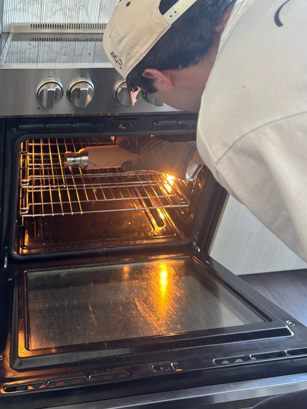 Leaning into an open oven, reaching in with an oven mitt for the cork-wrapped prototype on the rack